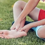 Young athlete in football kit holding their foot with heel pain after sport — a typical presentation of Sever's disease