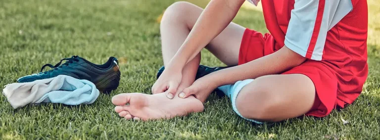 Child with heel pain after sport — Sever's disease Young athlete in football kit holding their foot with heel pain after sport — a typical presentation of Sever's disease