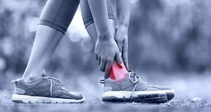 Runner clutching an ankle injury with red highlighted area indicating ankle sprain pain